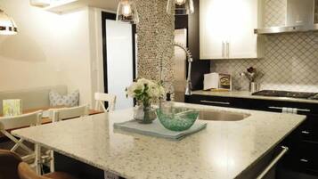 Una cocina con una isla grande, armarios blancos e iluminación colgante.