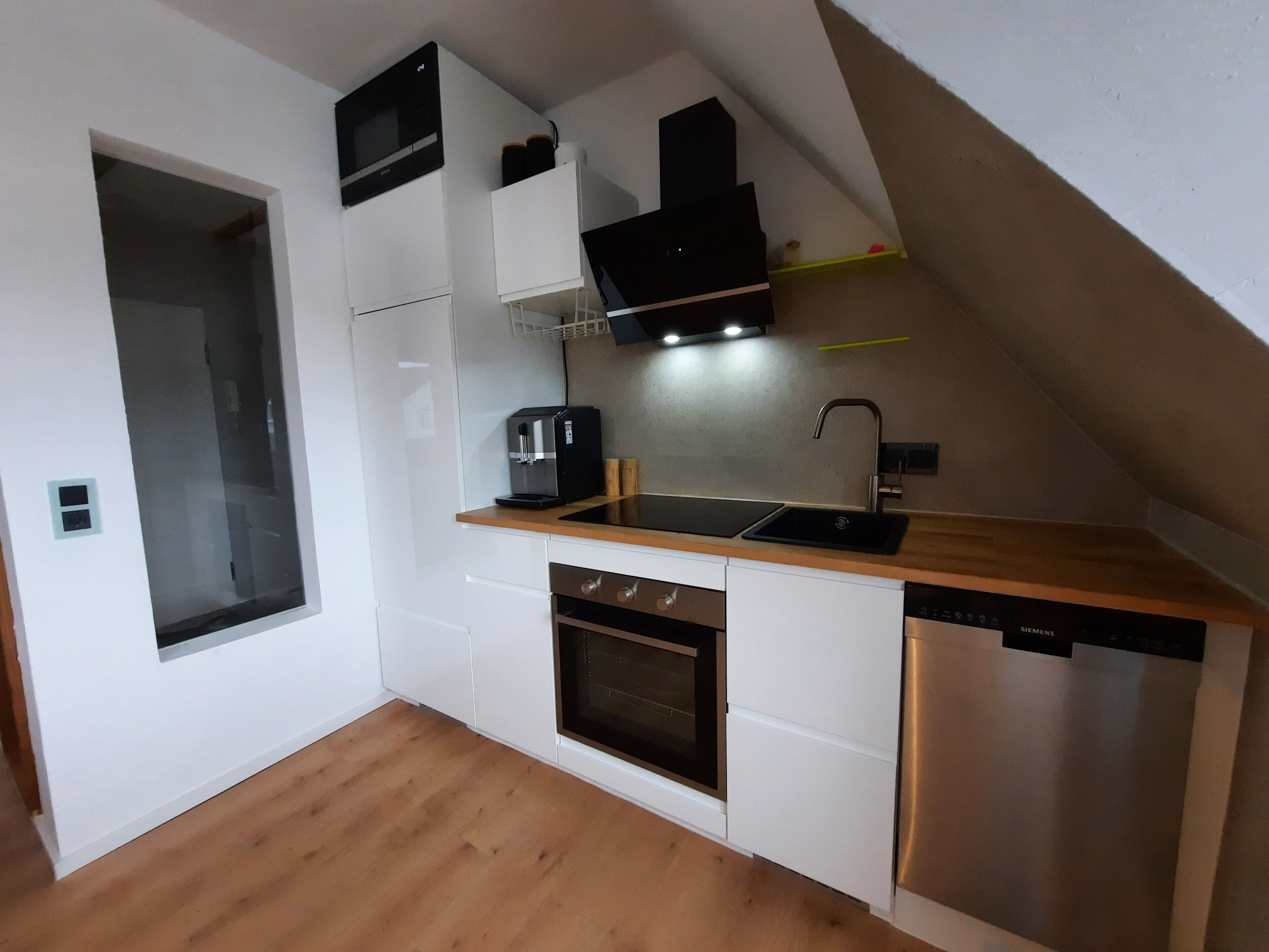 Una cocina compacta con gabinetes blancos, encimera de madera, horno integrado, lavavajillas y microondas.