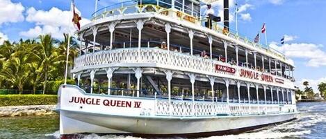 A double-decked river cruise ship named 'Jungle Queen IV' with multiple decks and passengers visible.