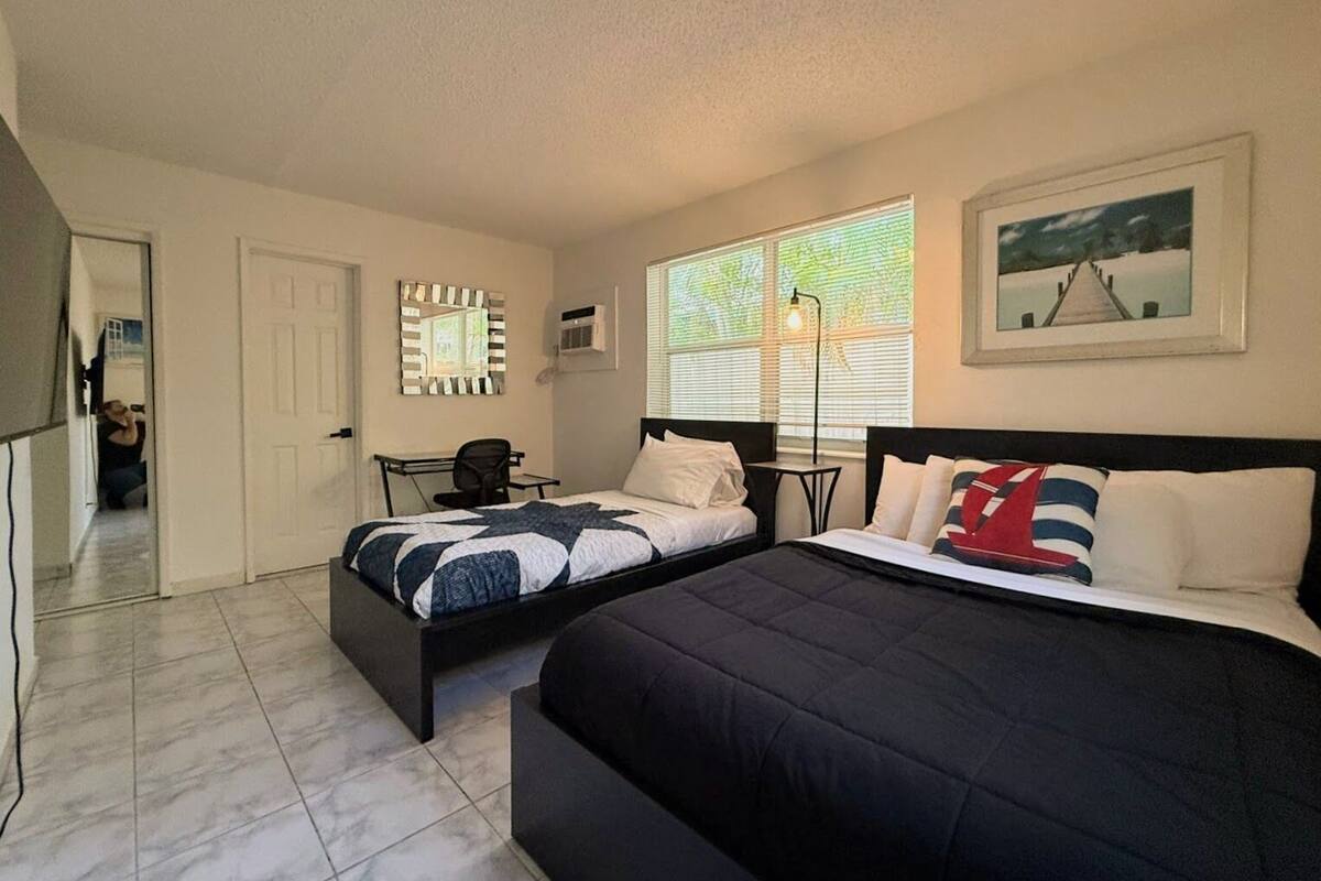 A bedroom with two beds, a desk, a chair, and a window with blinds.