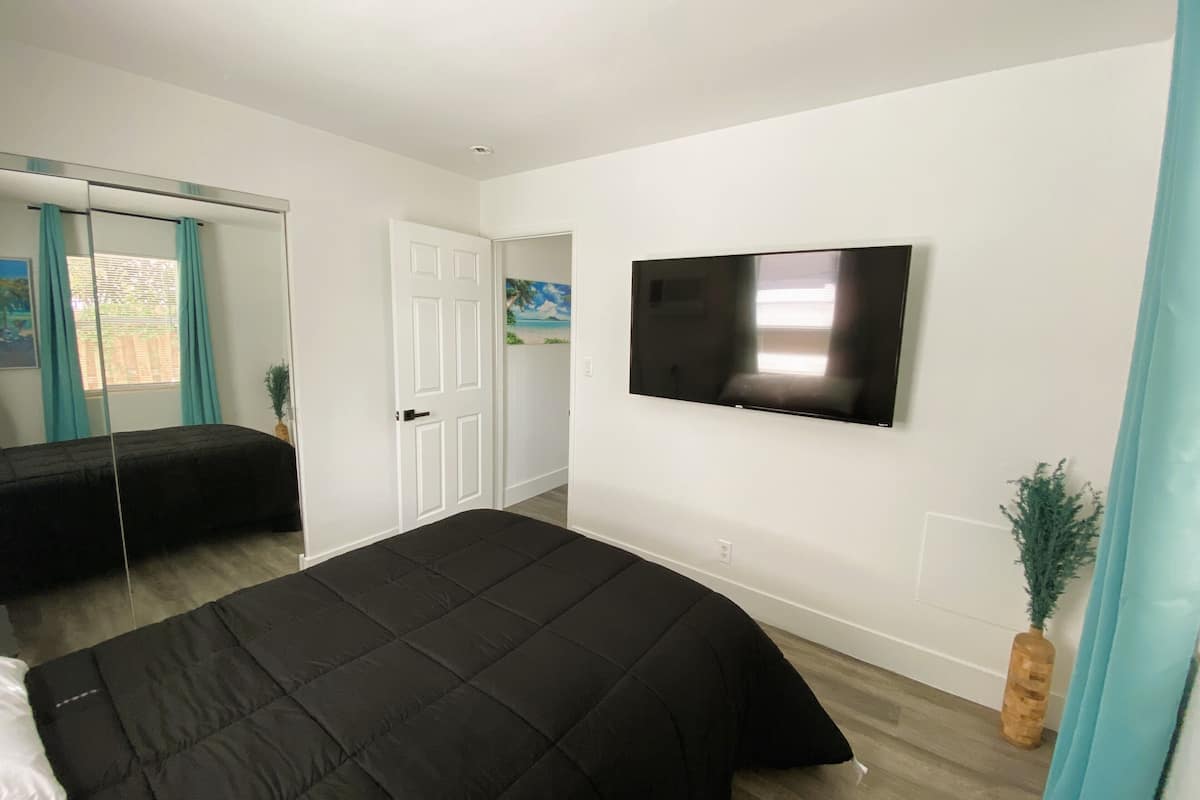 A bedroom with a bed, a TV mounted on the wall, and a door leading to another room.