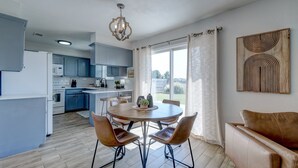 Cozinha moderna com armários azuis, mesa de jantar com quatro cadeiras e uma grande janela com cortinas.