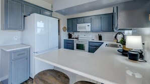 Uma cozinha moderna com armários azuis, bancadas brancas, micro-ondas embutido e fogão.
