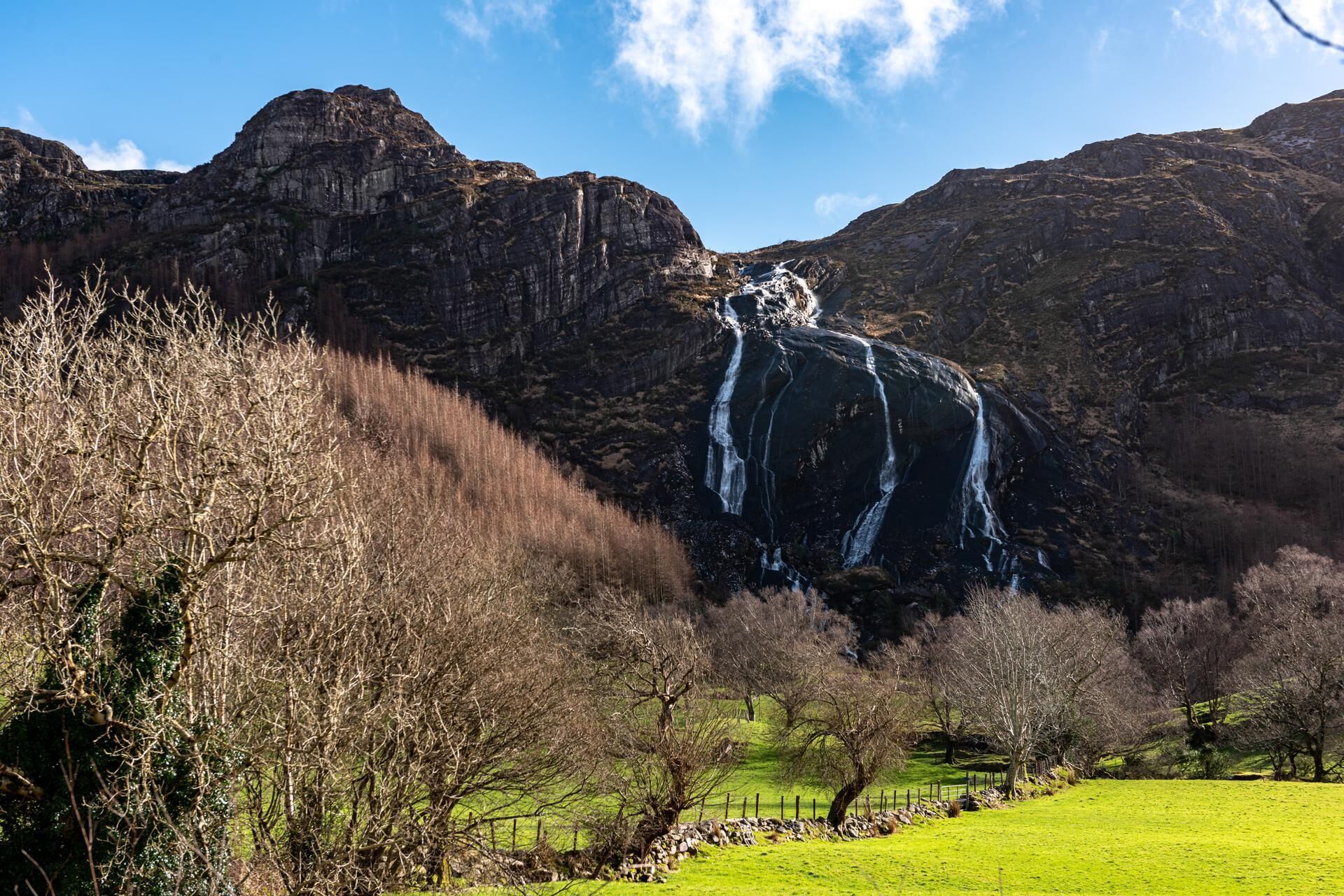 A waterfall cascading down a rocky cliff surrounded by a grassy field and trees.