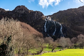 A waterfall cascading down a rocky cliff surrounded by a grassy field and trees.