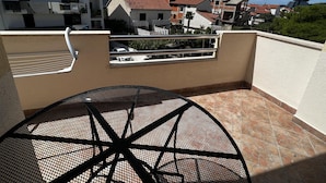 Un balcón con una mesa redonda de metal y barandilla, con vistas a una zona residencial con casas y cielo despejado.