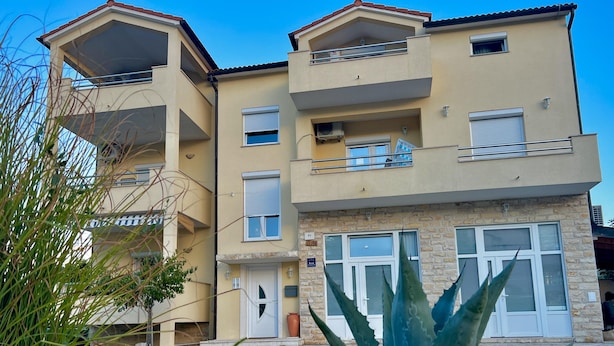 Un edificio residencial de varios pisos con balcones, fachada de piedra y cielo despejado.