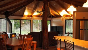 A rustic kitchen with a large dining table, bar stools, and a fireplace. - Blackwood Bush Retreat (Strathewen)