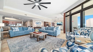 A spacious living area with a large ceiling fan, two sofas with patterned cushions, a coffee table, and a view of the kitchen and balcony. - Oasis, formerly Phoenix West II, New Owner, Beachfront and WaterSlide!! (Orange Beach)