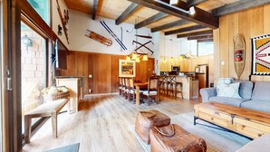A spacious living area with a wooden floor, a sofa, a dining table with chairs, and a kitchen area with wooden cabinets and a refrigerator.