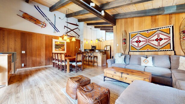 A rustic interior with wooden floors, a dining area with wooden chairs, a sofa, and a kitchen with wooden cabinets.