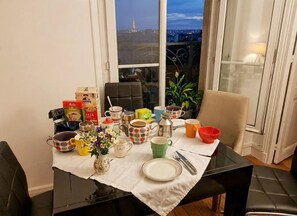 A dining table set with various mugs, plates, and a vase of flowers, with a view of the Eiffel Tower through a window. - AMAZING FLAT_WITH UNIQUE VIEW OF PARIS_MONTMARTRE (Paris)