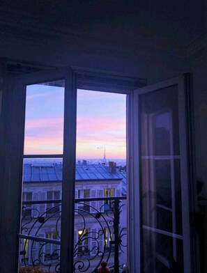 A room with a large window overlooking a cityscape at dusk.