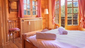 Ein Holzhütten-Zimmer mit einem Bett, einem Sessel, einer Heizung und Fenstern mit roten Karomustert-Vorhängen.