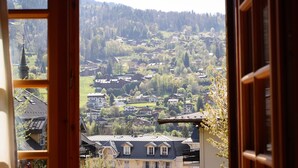 Blick durch ein Fenster auf eine Stadt mit Häusern, einer Kirche und einer Hügelkette im Hintergrund.
