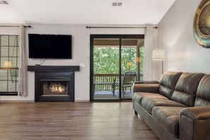 A living room with a fireplace, a sofa, a TV mounted on the wall, and a sliding glass door leading to an outdoor area. - Golf View Serenity - Open Deck - Close To Lake (Branson)