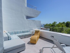 Um terraço no telhado com um sofá cinza claro, um banquinho amarelo e uma poltrona branca.