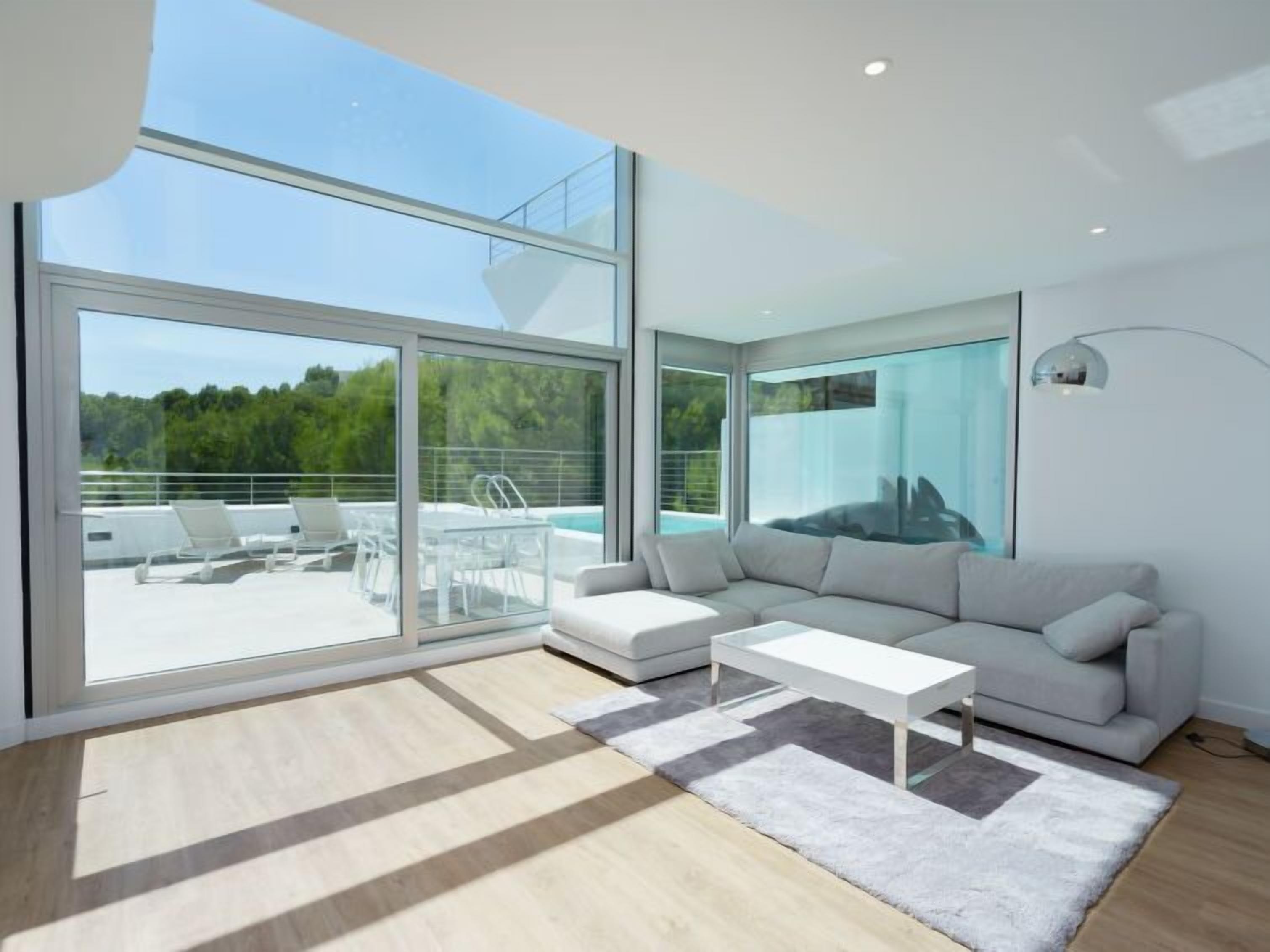 Sala de estar moderna com uma ampla parede de vidro, sofá branco, mesa de centro e vista para a piscina.