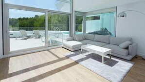 Un salon moderne doté d’un grand mur de verre, d’un canapé blanc, d’une table basse et offrant une vue sur la piscine.