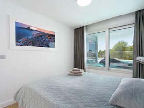 Quarto com cama, janela vista para piscina e pintura na parede.