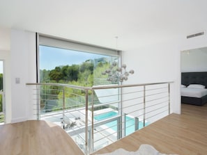 Quarto moderno com uma grande janela, varanda com piscina e vista para o verde.