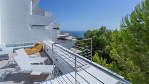 Un bâtiment moderne à l’extérieur blanc, doté d’une piscine sur le toit et d’un espace détente avec des chaises longues, offrant une vue dégagée sur la mer.
