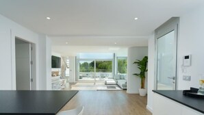 Une cuisine moderne avec un plan de travail noir, des armoires blanches et un plancher en bois. On y trouve un coin repas avec des chaises blanches et une grande fenêtre donnant sur un balcon.