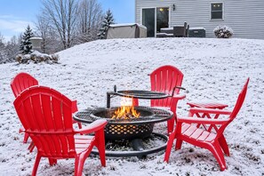 Een besneeuwde buitenruimte met een vuurkorf en rode stoelen.