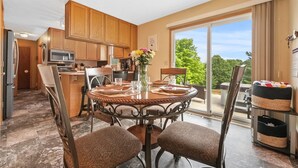 Een moderne keuken met houten kastjes, een eettafel gedekt voor vier personen en een grote schuifdeur naar een balkon met uitzicht op groen.