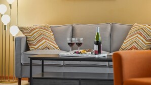 Een moderne woonkamer met een grijze bank, gestreepte kussens, een bijzettafeltje met een fles wijn, glazen en snacks.