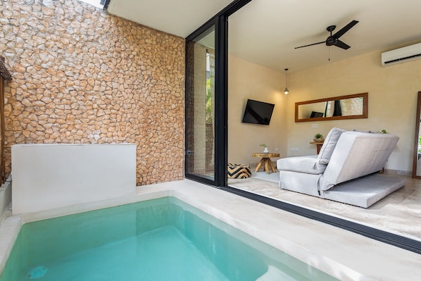 A modern bathroom with a stone wall, a bathtub, and a seating area with a sofa and a small table.