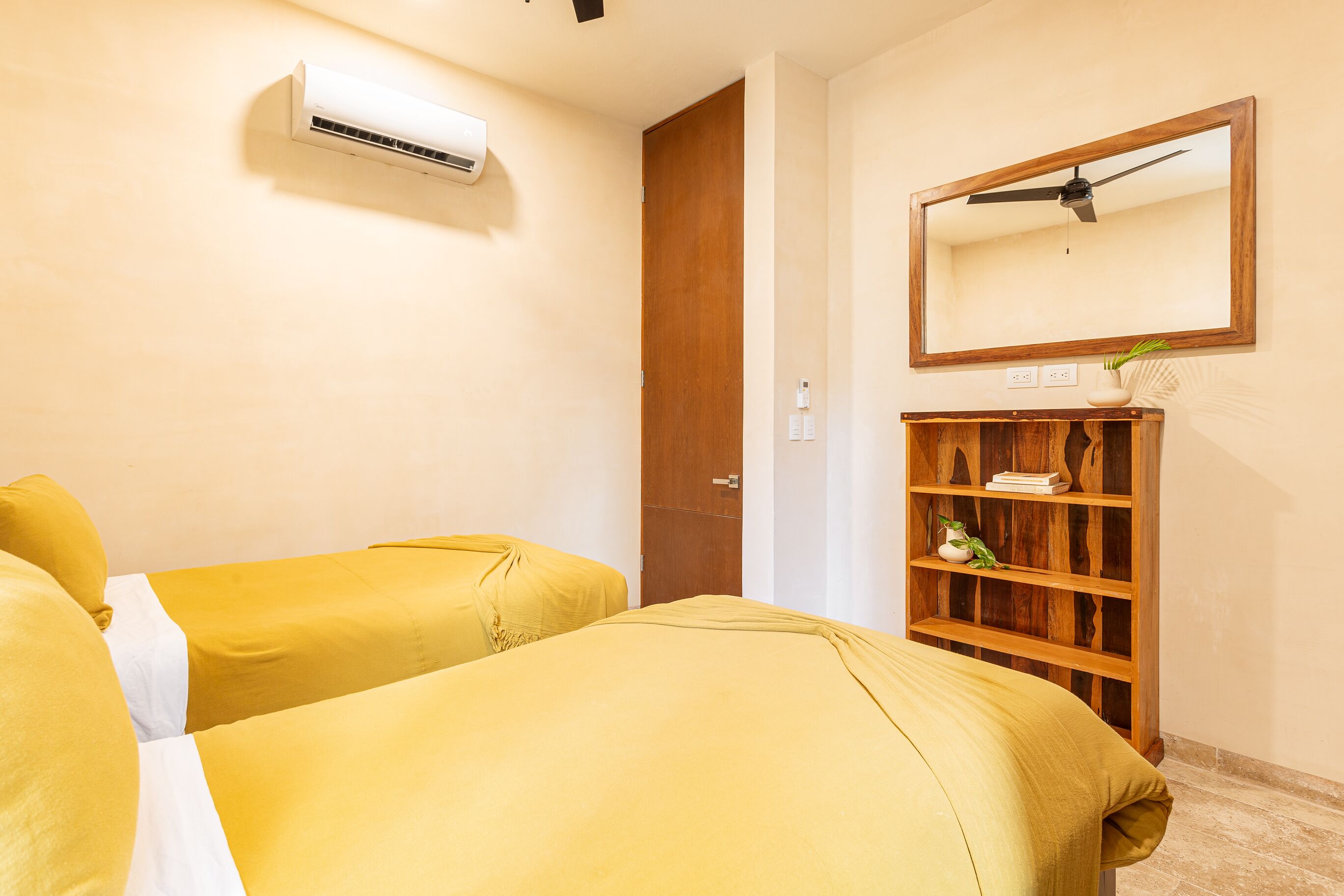 Quarto de hotel com duas camas, ar condicionado, uma estante de madeira e um espelho na parede.