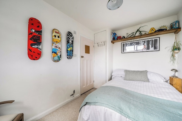 A bedroom with a bed, a wall-mounted shelf with books and decorative items, and three skateboards on the wall.