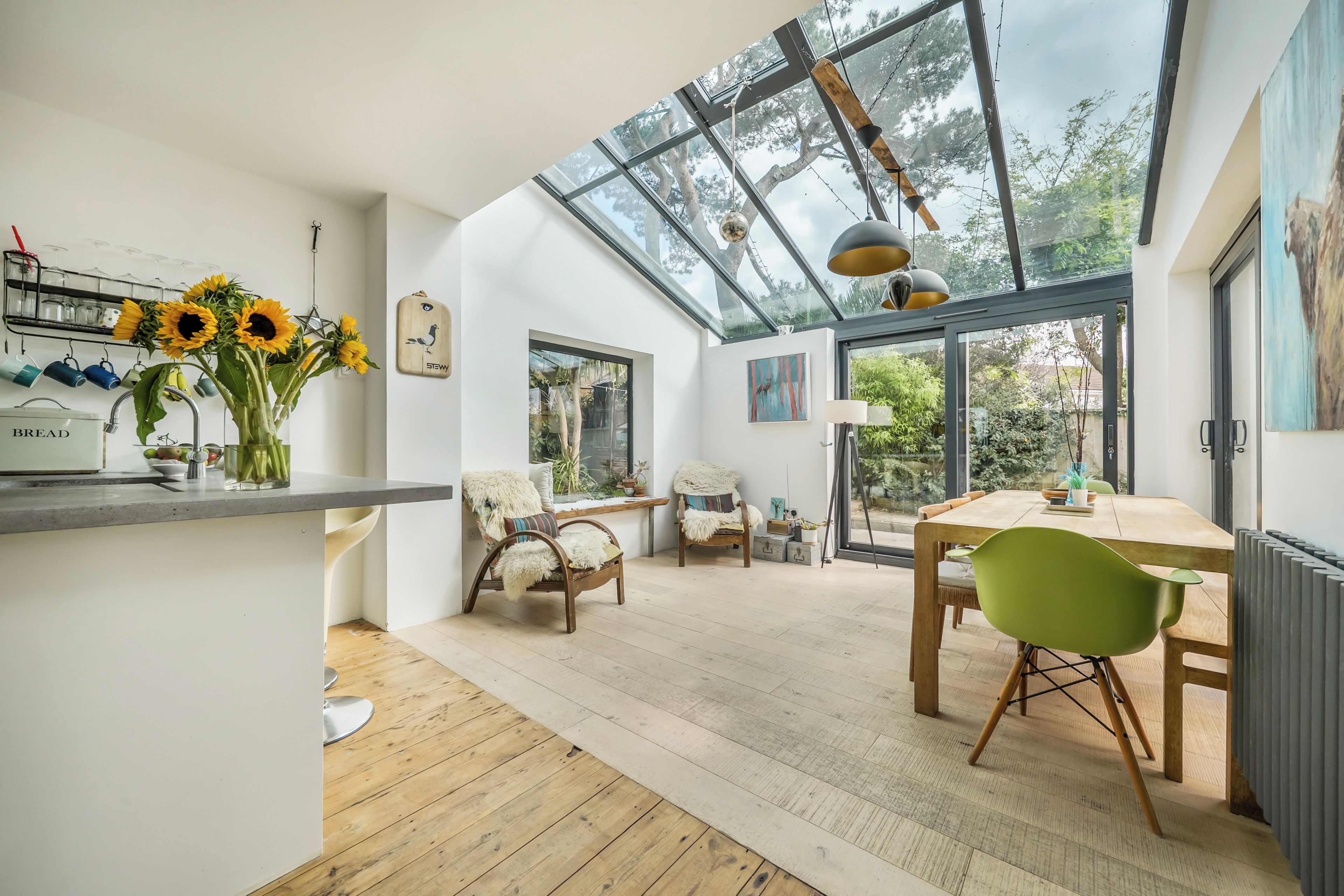 A spacious kitchen with a large skylight, wooden flooring, and a dining area with a table and chairs.