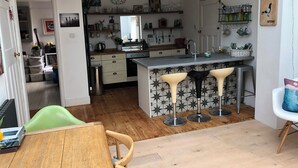 A modern kitchen with a central island, bar stools, and a dining area with a wooden table and chairs. - 5 Bed House - Sleeps 15 - Pets - Garden - Parking (Kingsbridge)