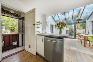 A modern kitchen with a dishwasher, a dining area with a table and chairs, and a large window with a view of greenery.