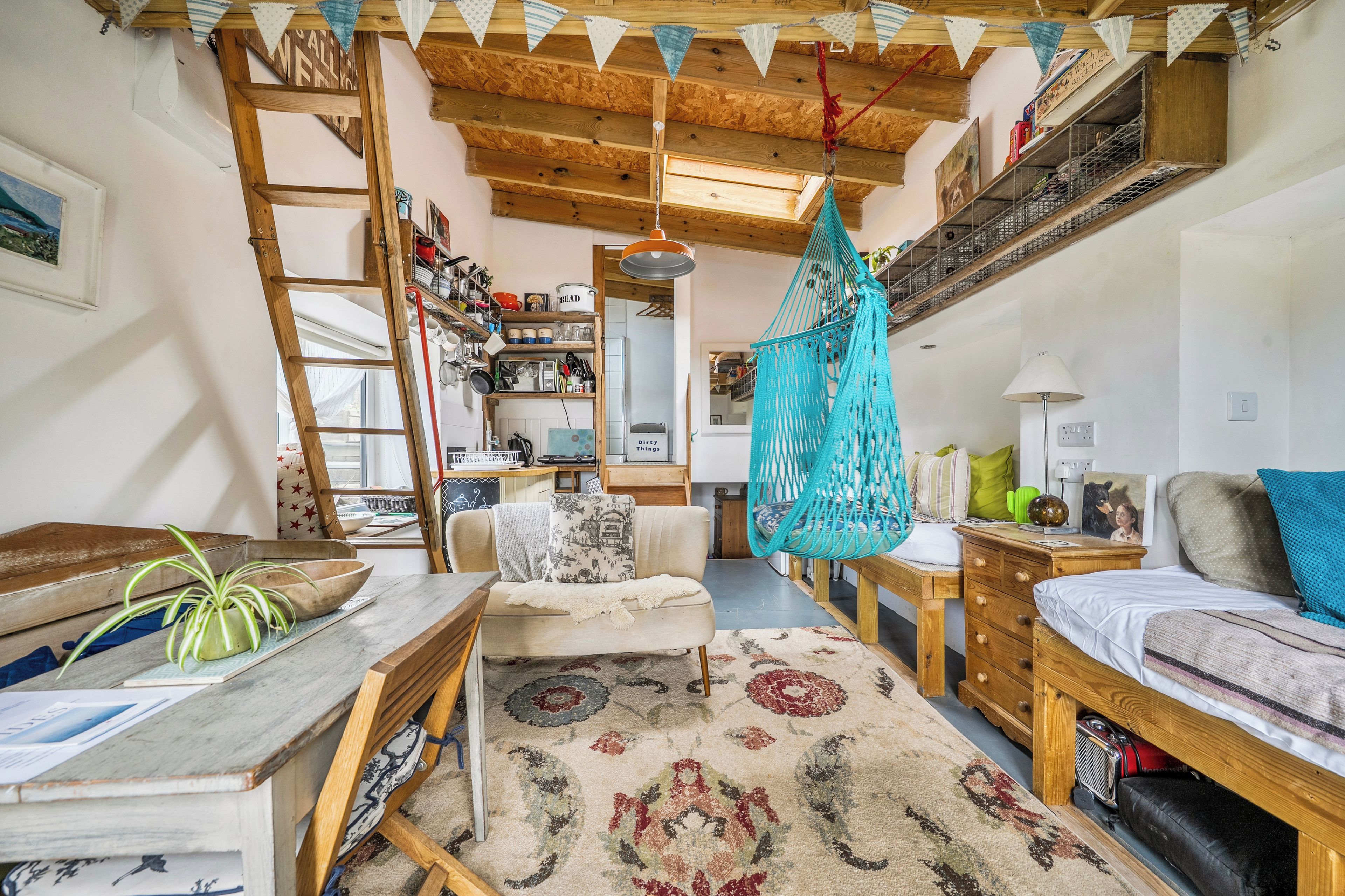 Une pièce chaleureuse et rustique, dotée d’un lit en mezzanine, d’un fauteuil suspendu en macramé et d’une échelle en bois.