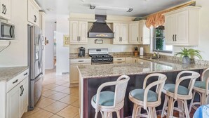 A spacious kitchen with white cabinets, a large island with bar stools, stainless steel appliances, and a central range hood. - Bayfront to Beach Beauty Access to bay (Dewey Beach)