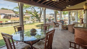 A covered patio with a glass table and wicker chairs, overlooking a grassy area and a canal. - Bayfront to Beach Beauty Access to bay (Dewey Beach)