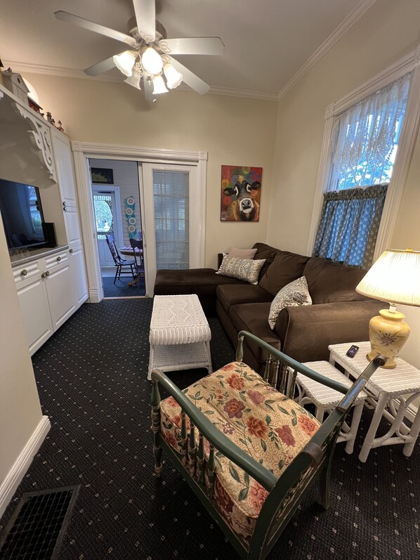 A living room with a brown sofa, white armchairs, a small white table, a ceiling fan, and a TV on a cabinet. - Charming Victorian, Private Hot Tub (New Buffalo)