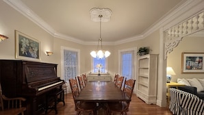 A dining room with a long wooden table, chairs, a piano, and a chandelier. - Charming Victorian, Private Hot Tub (New Buffalo)