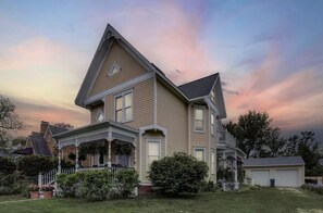 Une maison à deux étages avec une véranda qui fait le tour de la maison, un garage et une pelouse bien entretenue.