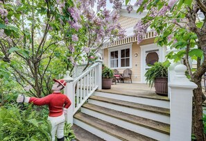 A wooden staircase leading to a porch with a white railing, surrounded by lush greenery and flowering trees. - Charming Victorian, Private Hot Tub (New Buffalo)