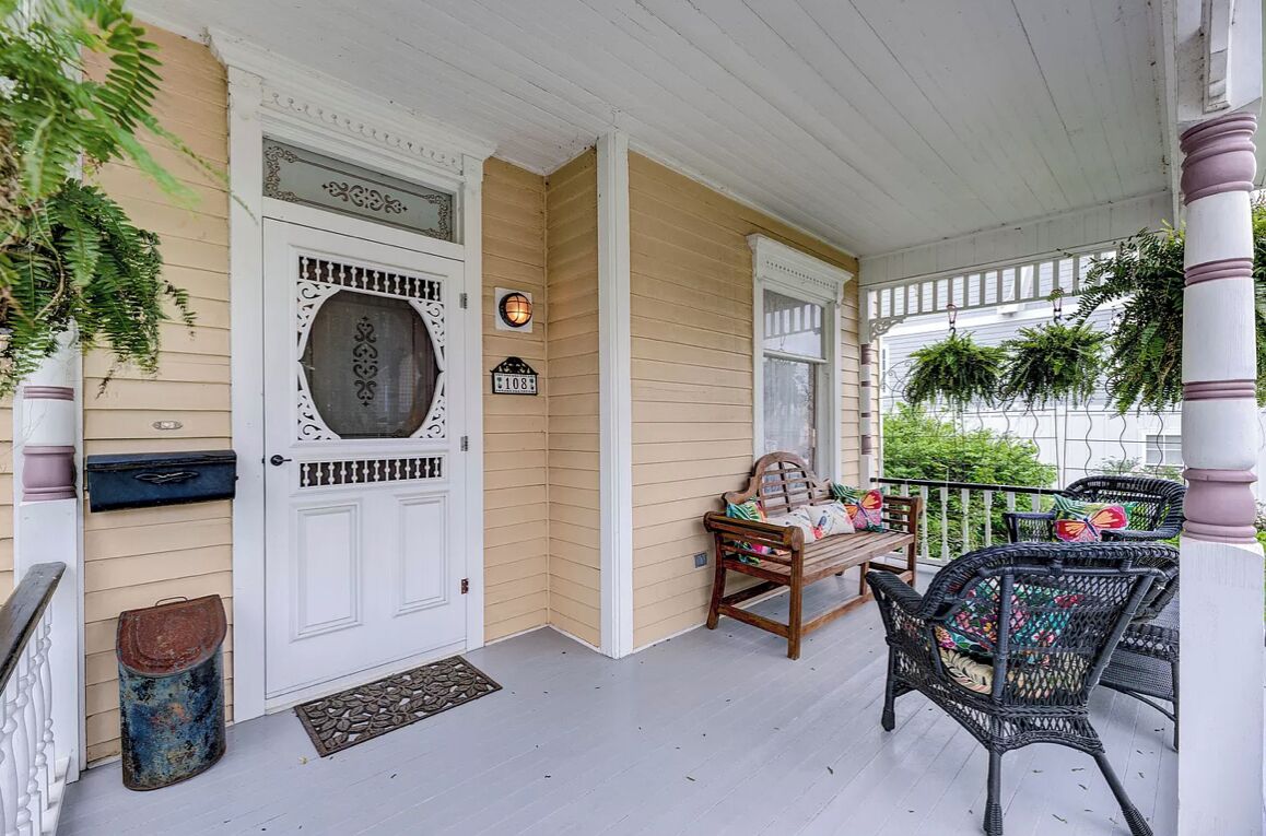 A porch with a white door, a bench, and wicker chairs.