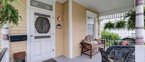 A porch with a white door, a bench, and wicker chairs.