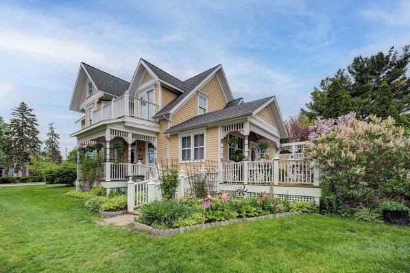 A two-story house with a wrap-around porch, a small garden, and a white fence.