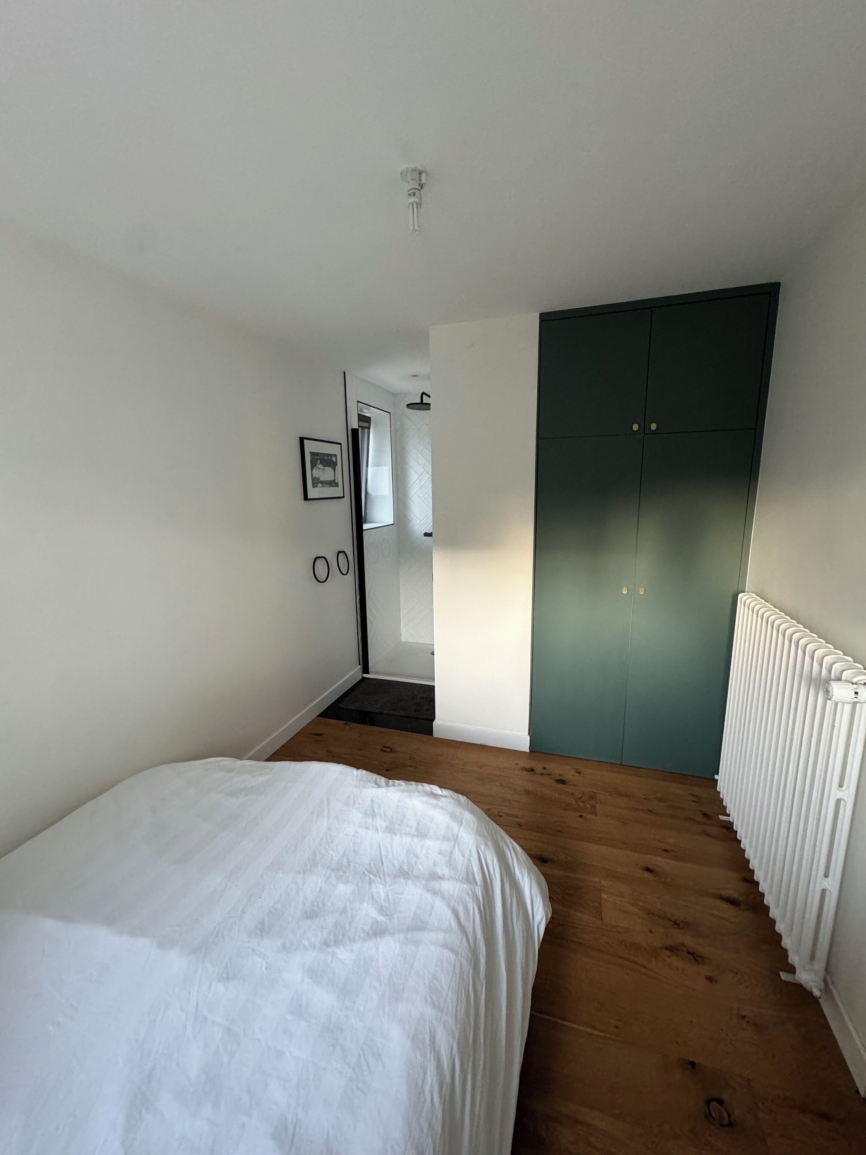 Een slaapkamer met een bed, houten vloeren, een radiator en een groene garderobe.