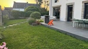 Ein modernes Haus mit Terrasse, kleinem Garten und Essbereich mit Gartenmöbeln.