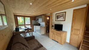 A cozy cabin interior with a wooden ceiling, a sofa, a TV, a kitchen area, and a dining table. - Chalet, Ground floor, parking, tv, ski locker, 44m², Le Grand Bornand (Le Grand-Bornand)
