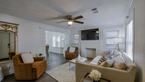 A spacious living room with a fireplace, a ceiling fan, and a large mirror.